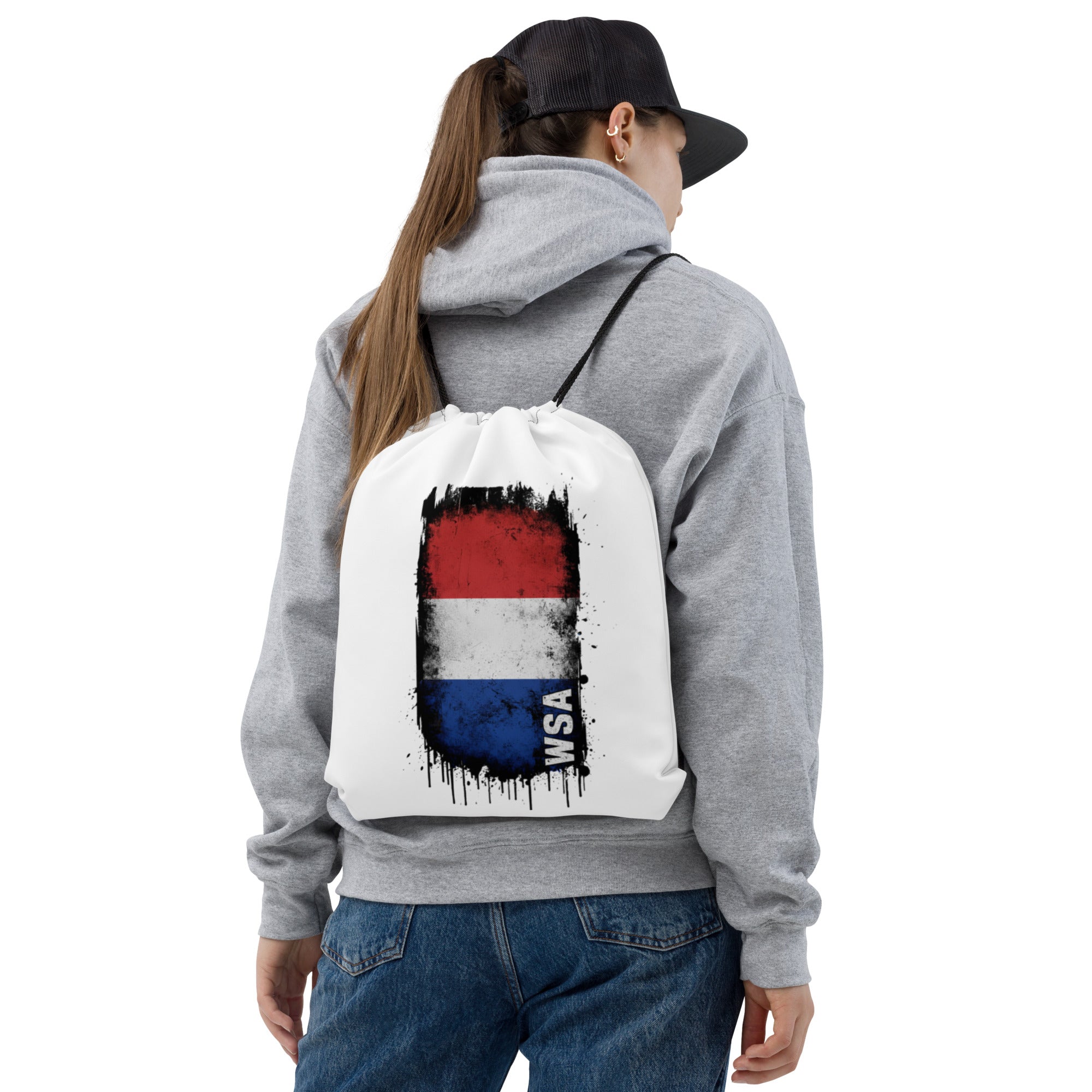 Person wearing a gray hoodie and blue jeans with a white drawstring bag featuring a colorful design on the back.