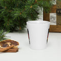 White mug with festive design on a white surface with Christmas decorations.