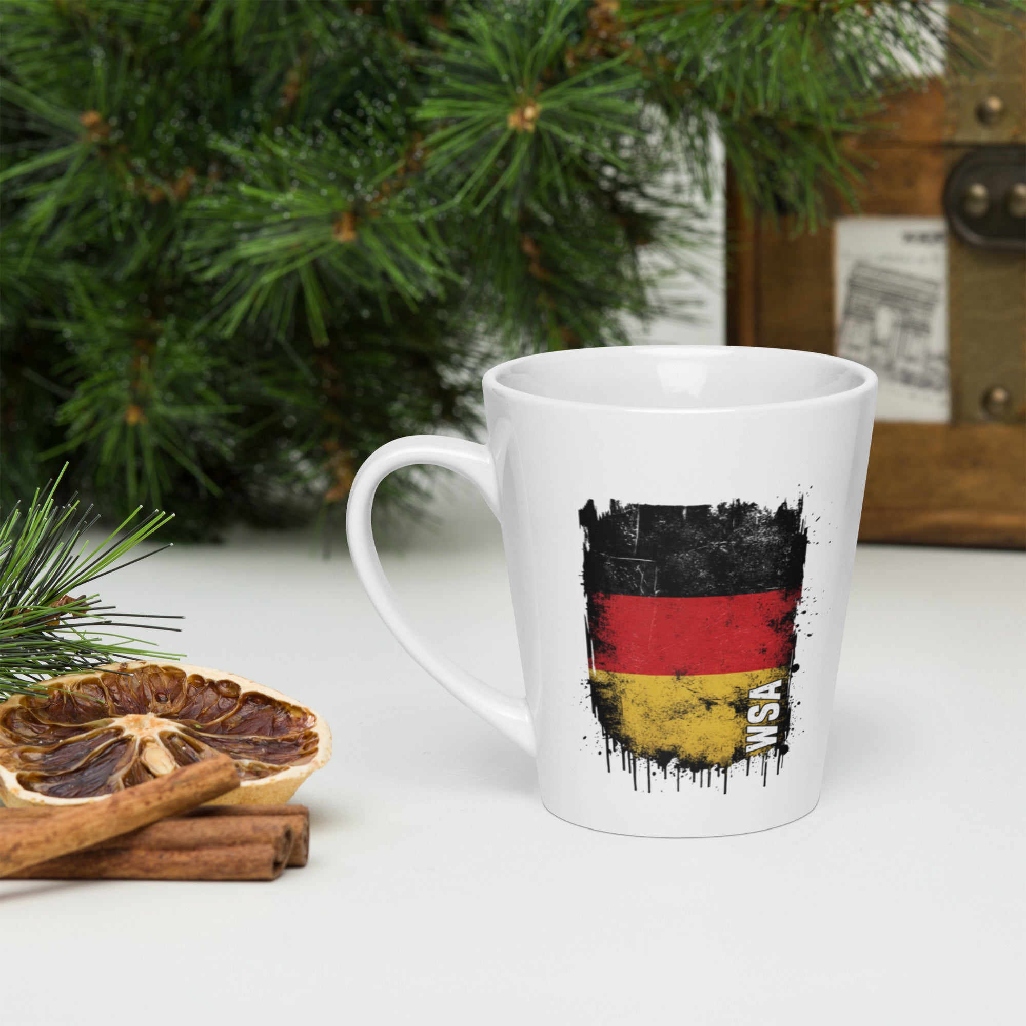 White mug with German flag design on a table with Christmas decorations.
