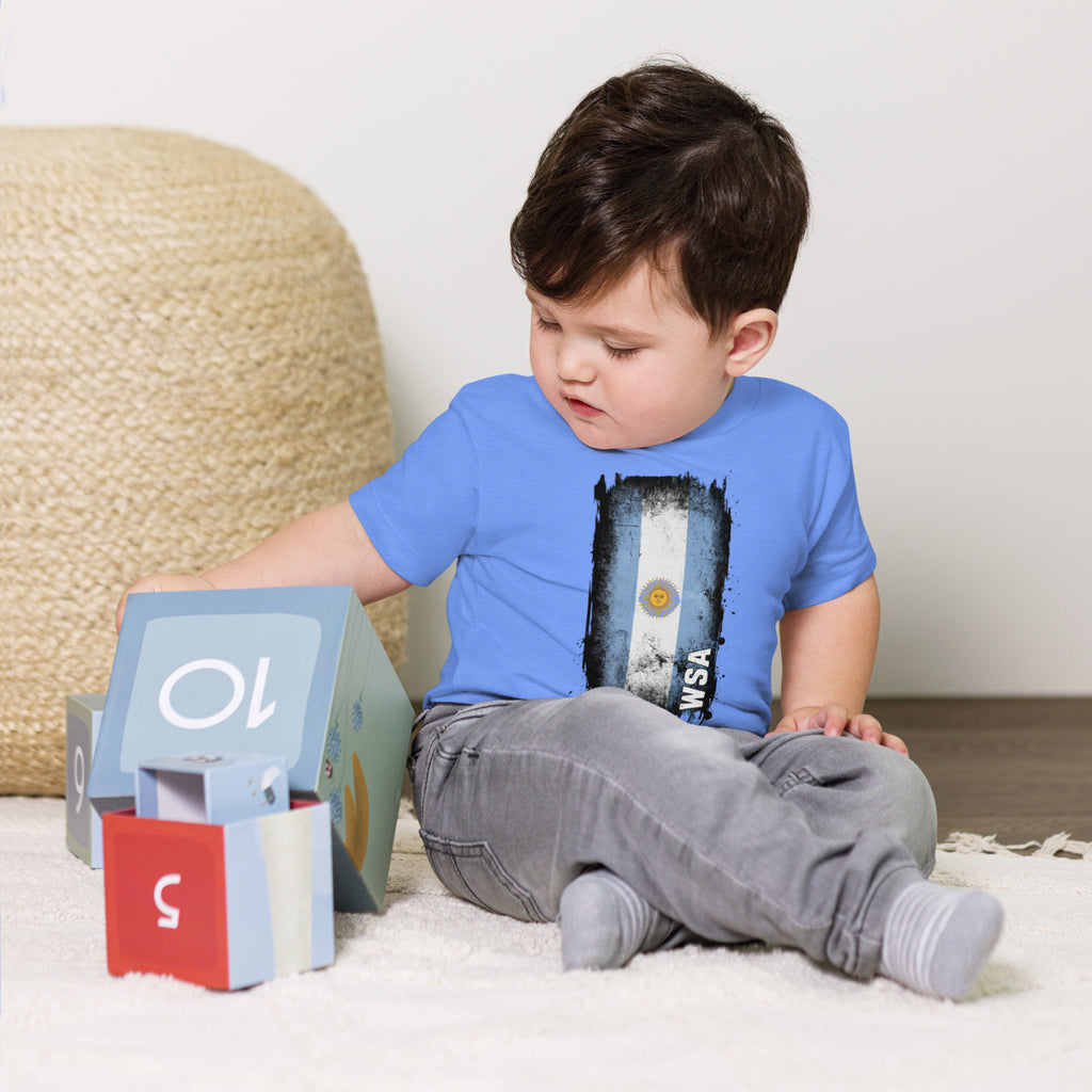 Child wearing a blue t-shirt with a graphic design, sitting on a carpeted floor.