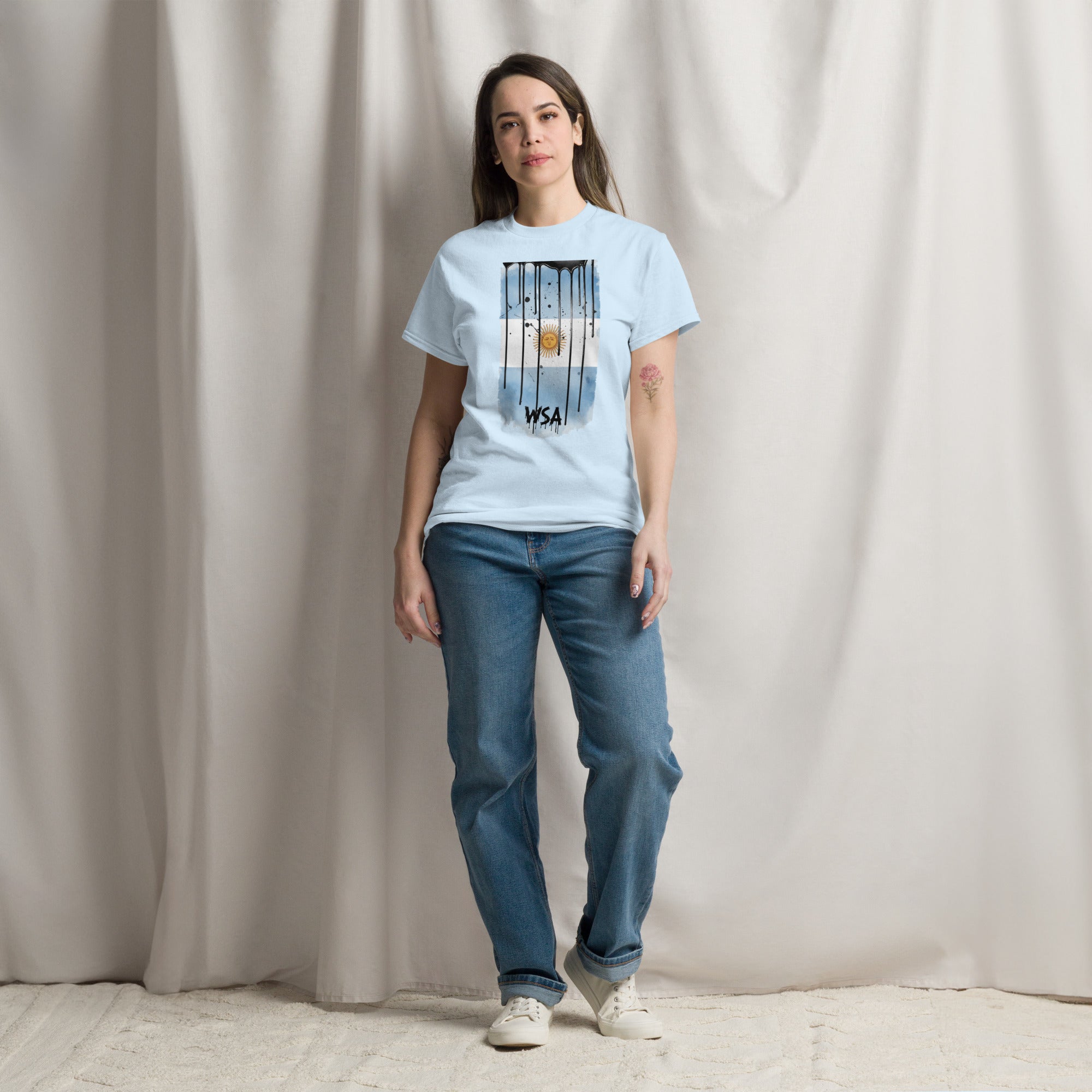 Woman wearing a light blue t-shirt and jeans standing against a plain background