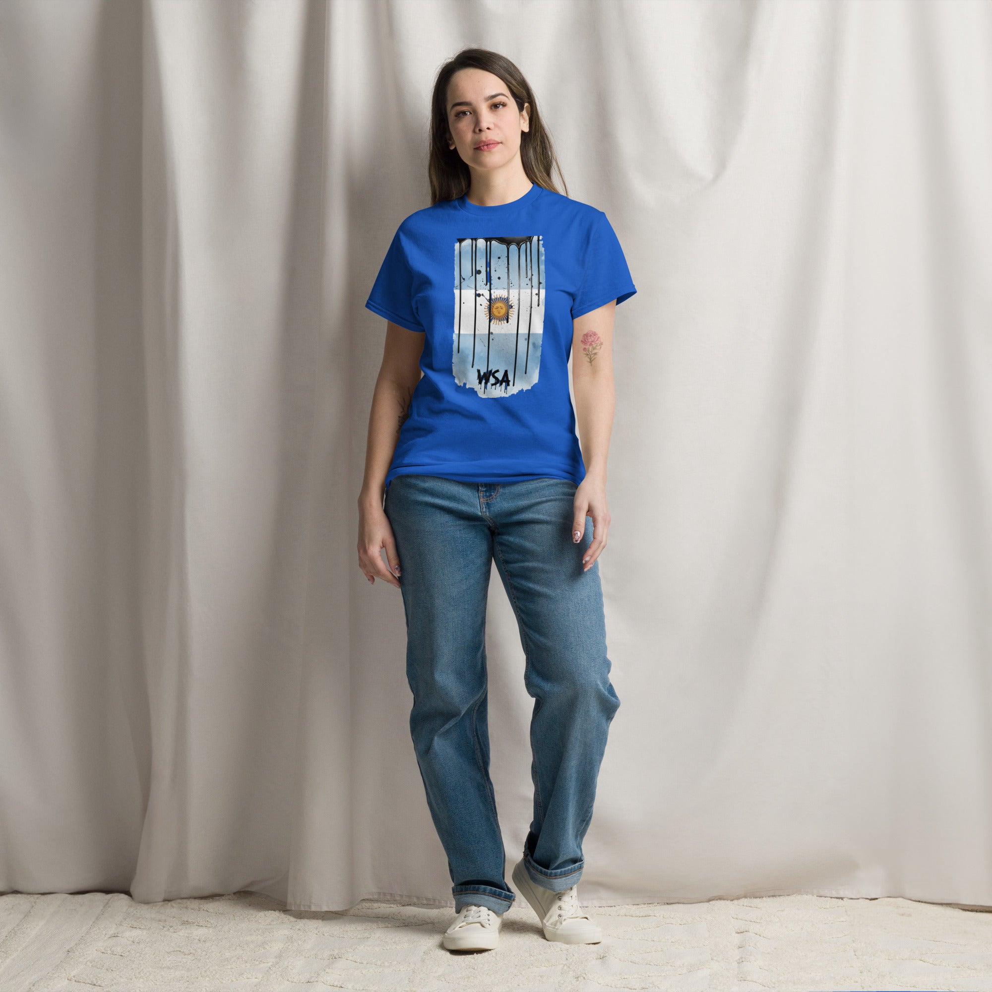 Person wearing a blue t-shirt with a graphic design and jeans standing against a plain background