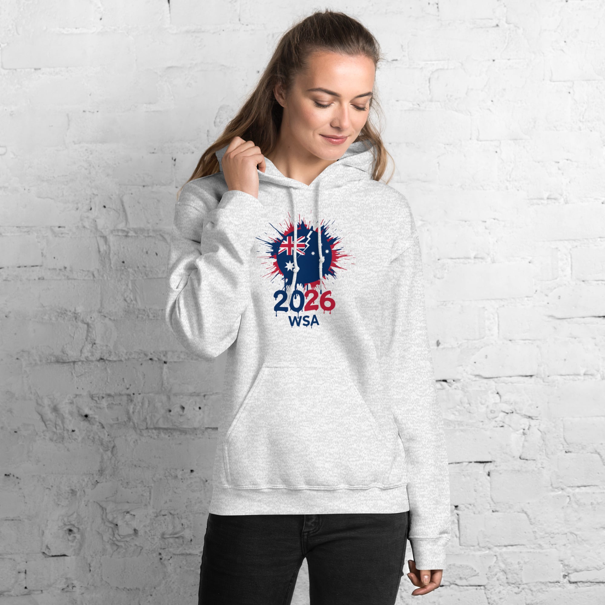 Woman wearing a white hoodie with a design and text against a white brick wall.