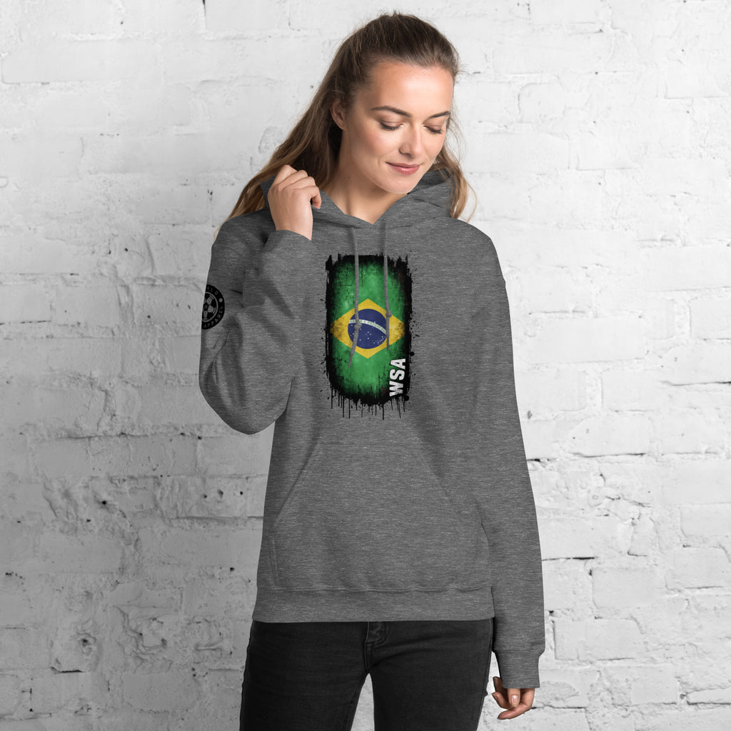 Person wearing a gray hoodie with a Brazilian flag design against a white brick wall.