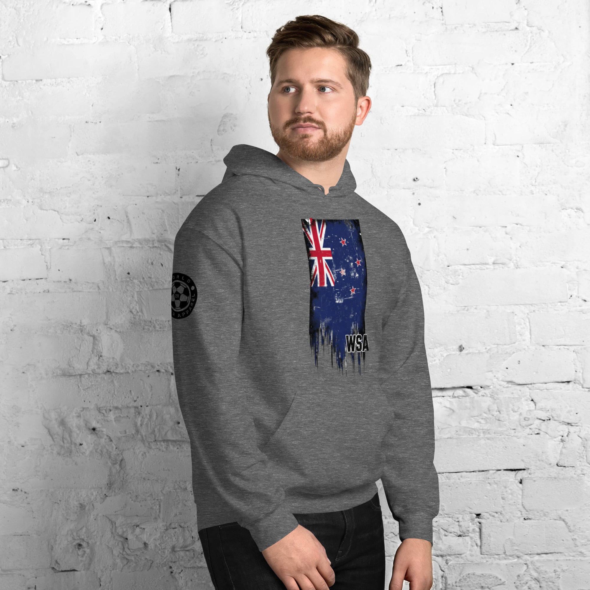 Man wearing a gray hoodie with a flag design against a white brick wall.