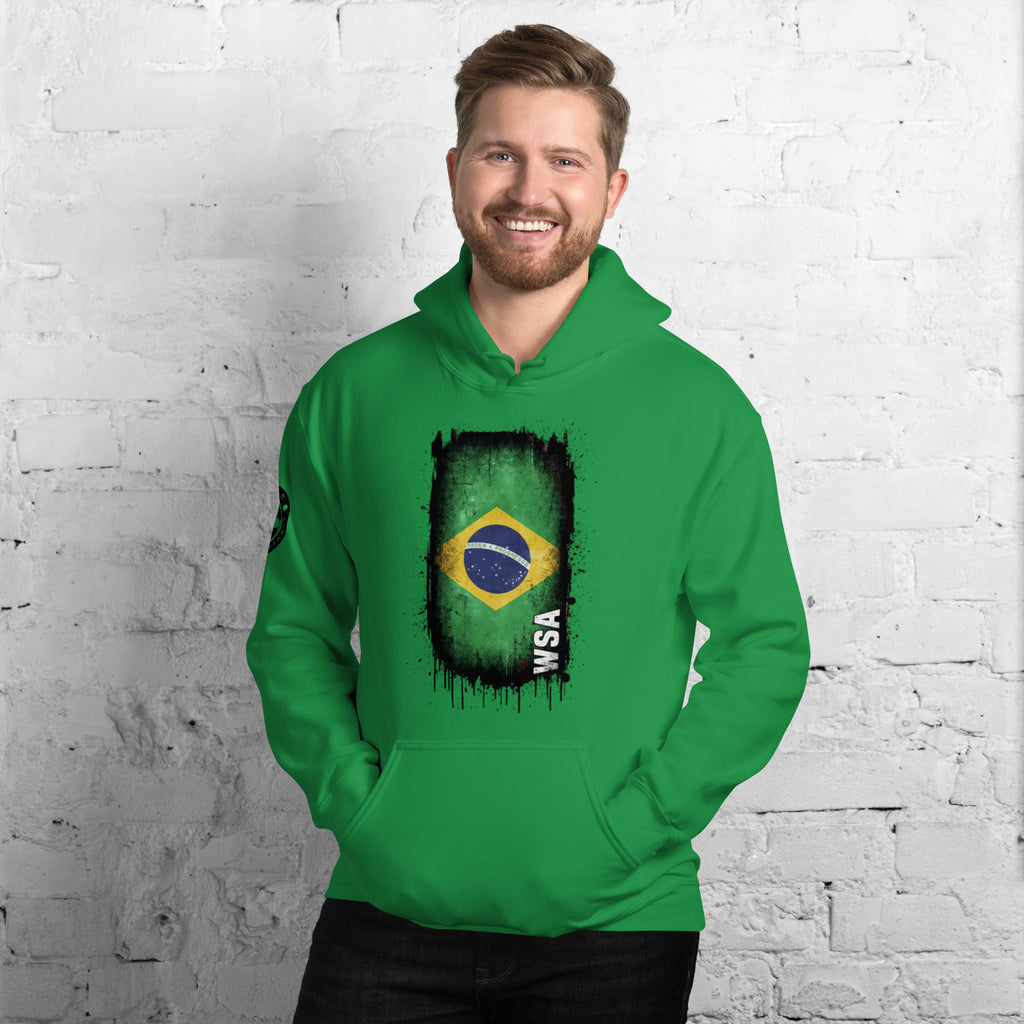Man wearing a green hoodie with a flag design against a white brick wall.
