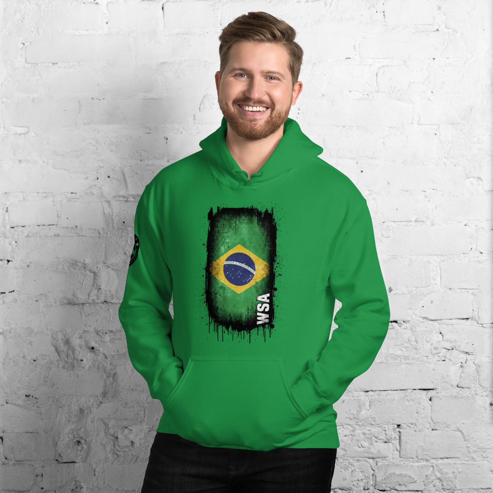 Man wearing a green hoodie with a flag design against a white brick wall.