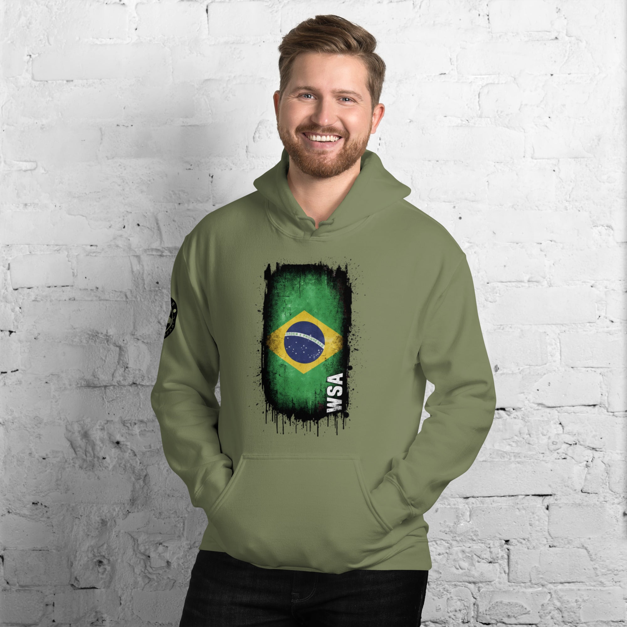 Man wearing a green hoodie with a flag design against a white brick wall.