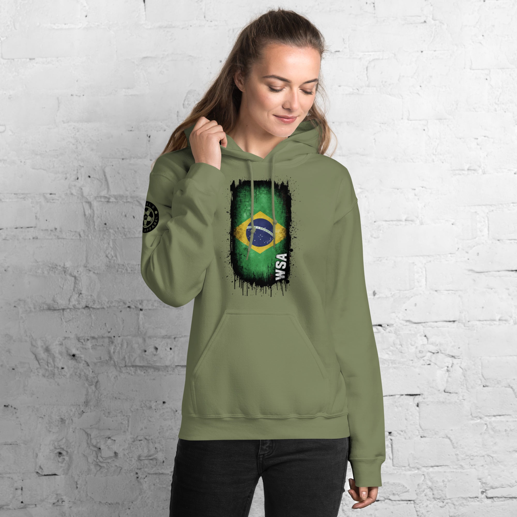 Person wearing a green hoodie with a Brazilian flag design against a white brick wall.