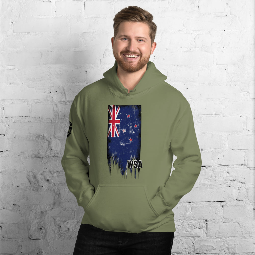 Man wearing a green hoodie with a New Zealand flag design against a white brick wall.