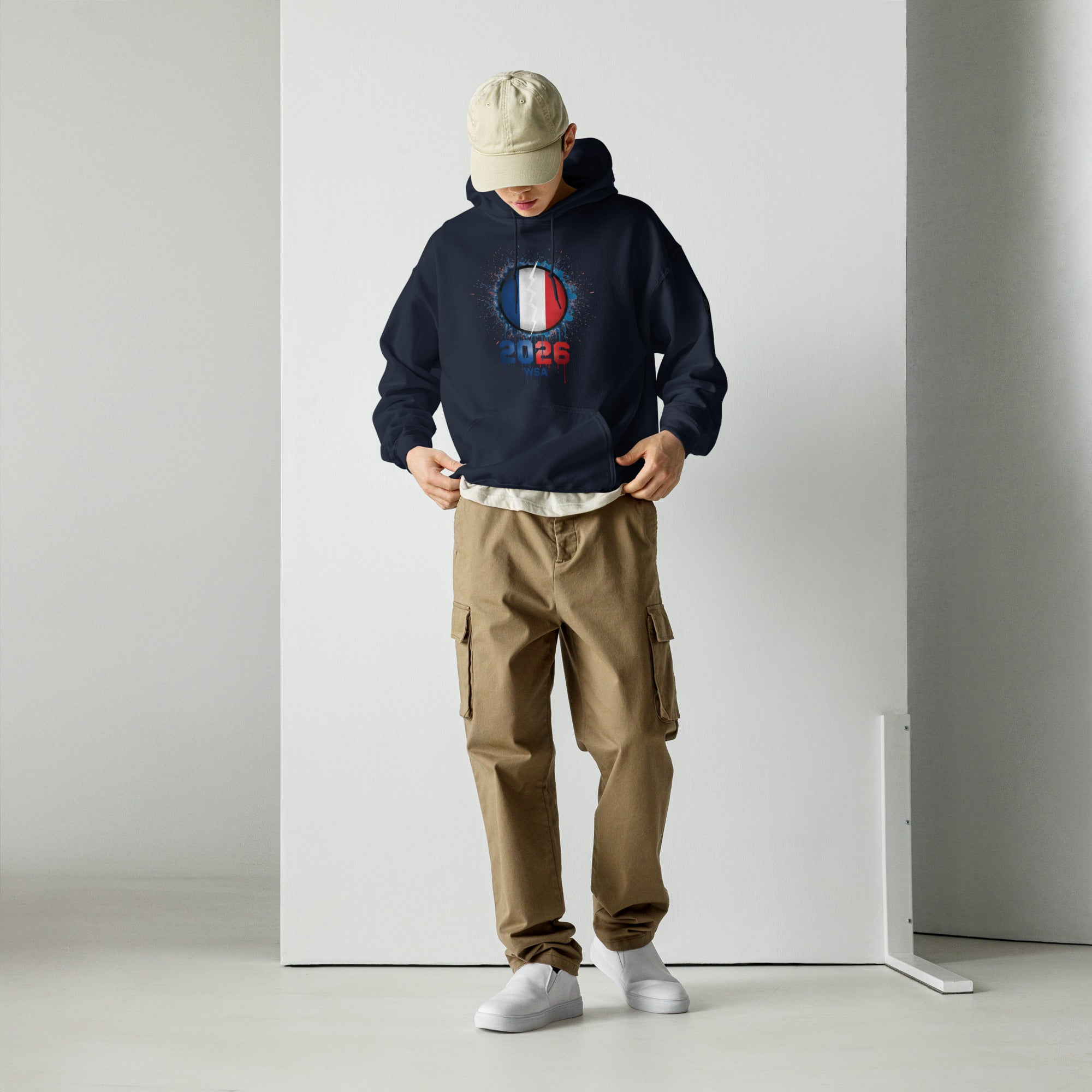 Person wearing a navy hoodie with a graphic design, beige cap, and brown cargo pants against a white background.