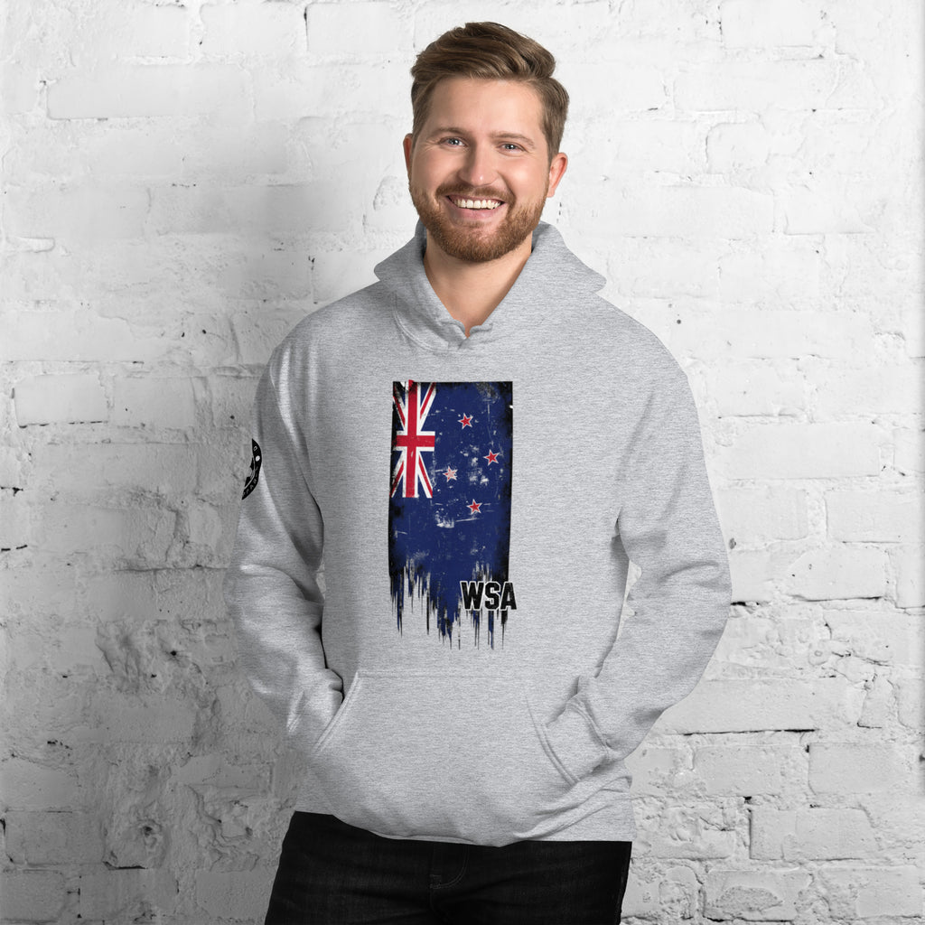 Man wearing a gray hoodie with a New Zealand flag design against a white brick wall.