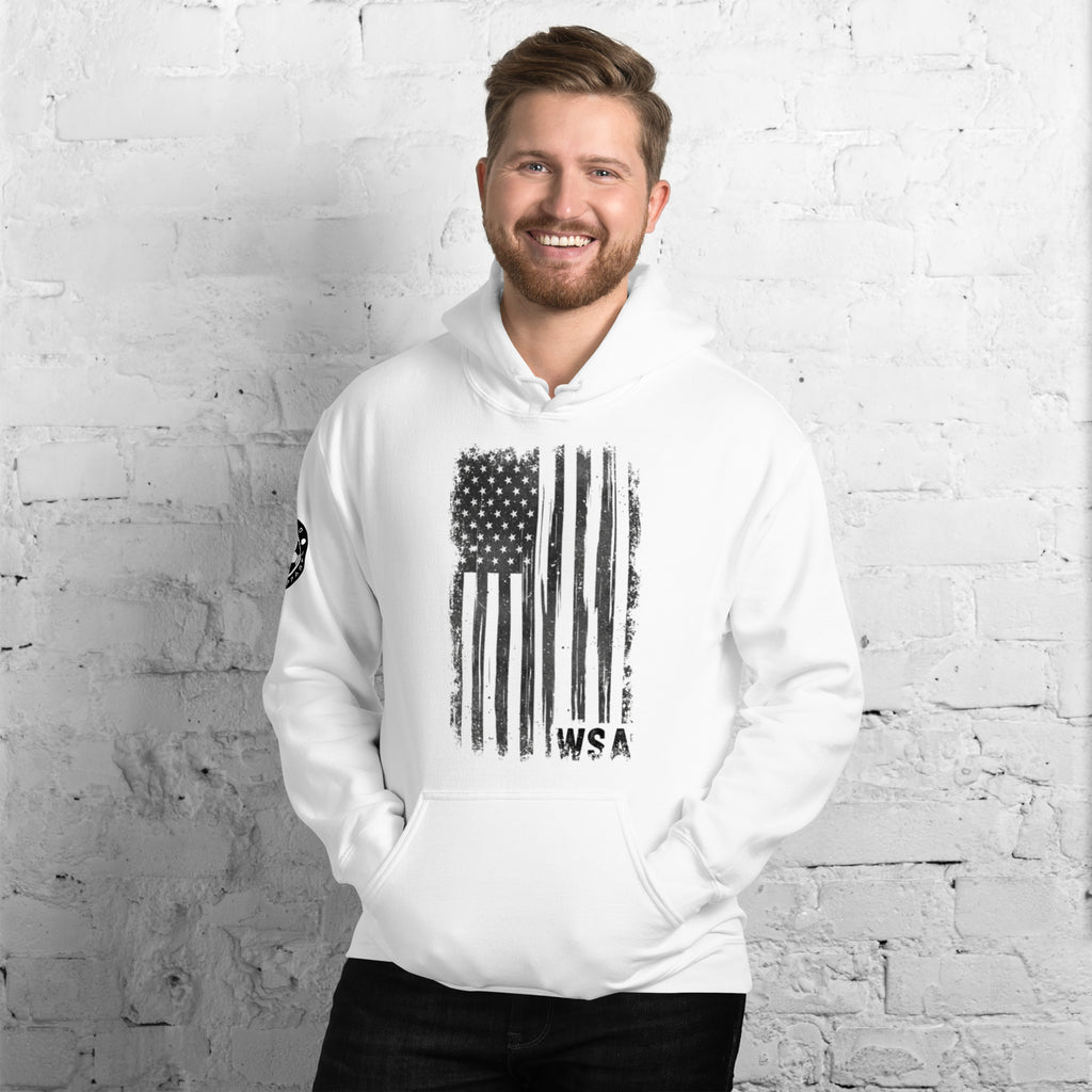 Man wearing a white hoodie with an American flag design against a white brick wall.