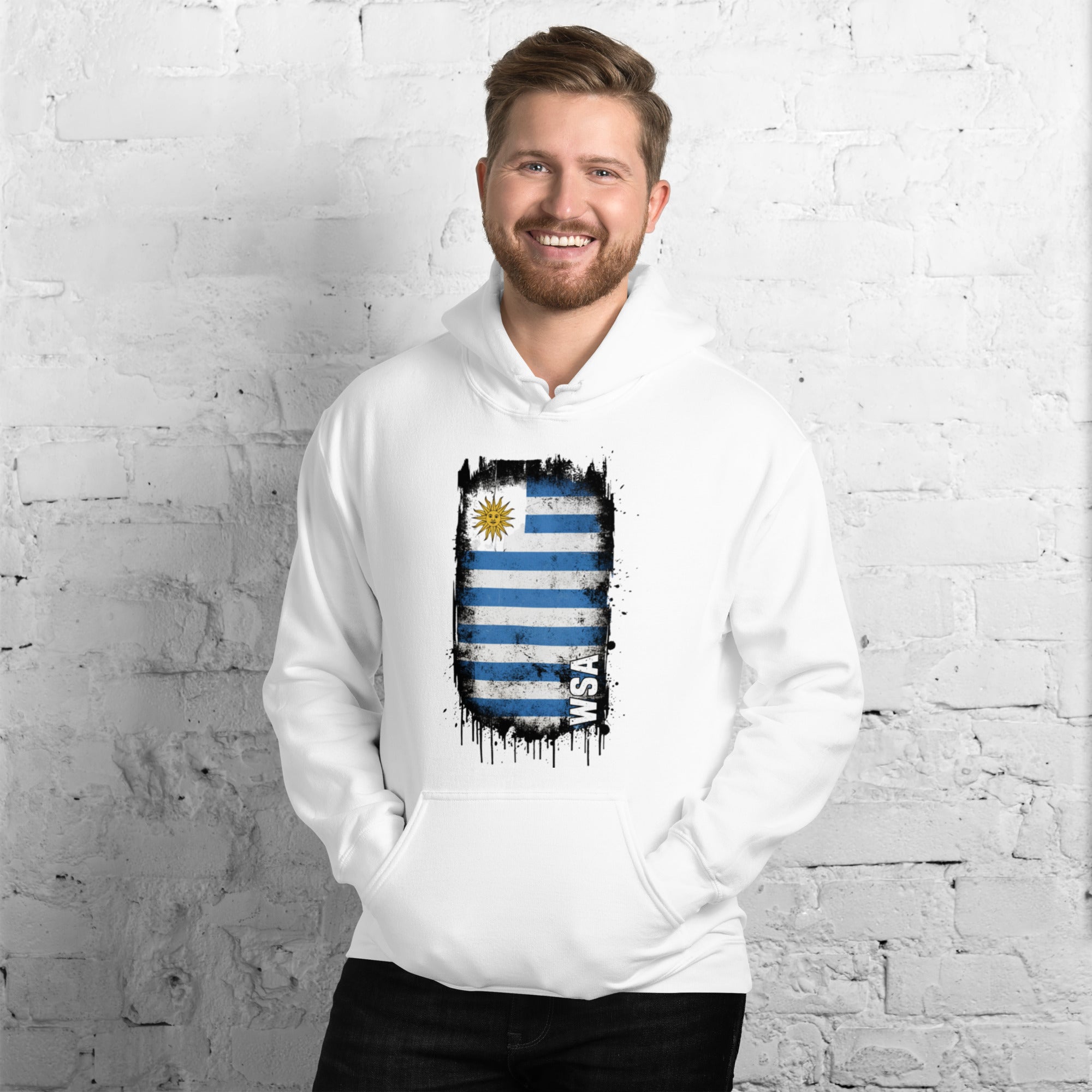 Man wearing a white hoodie with a flag design against a white brick wall.