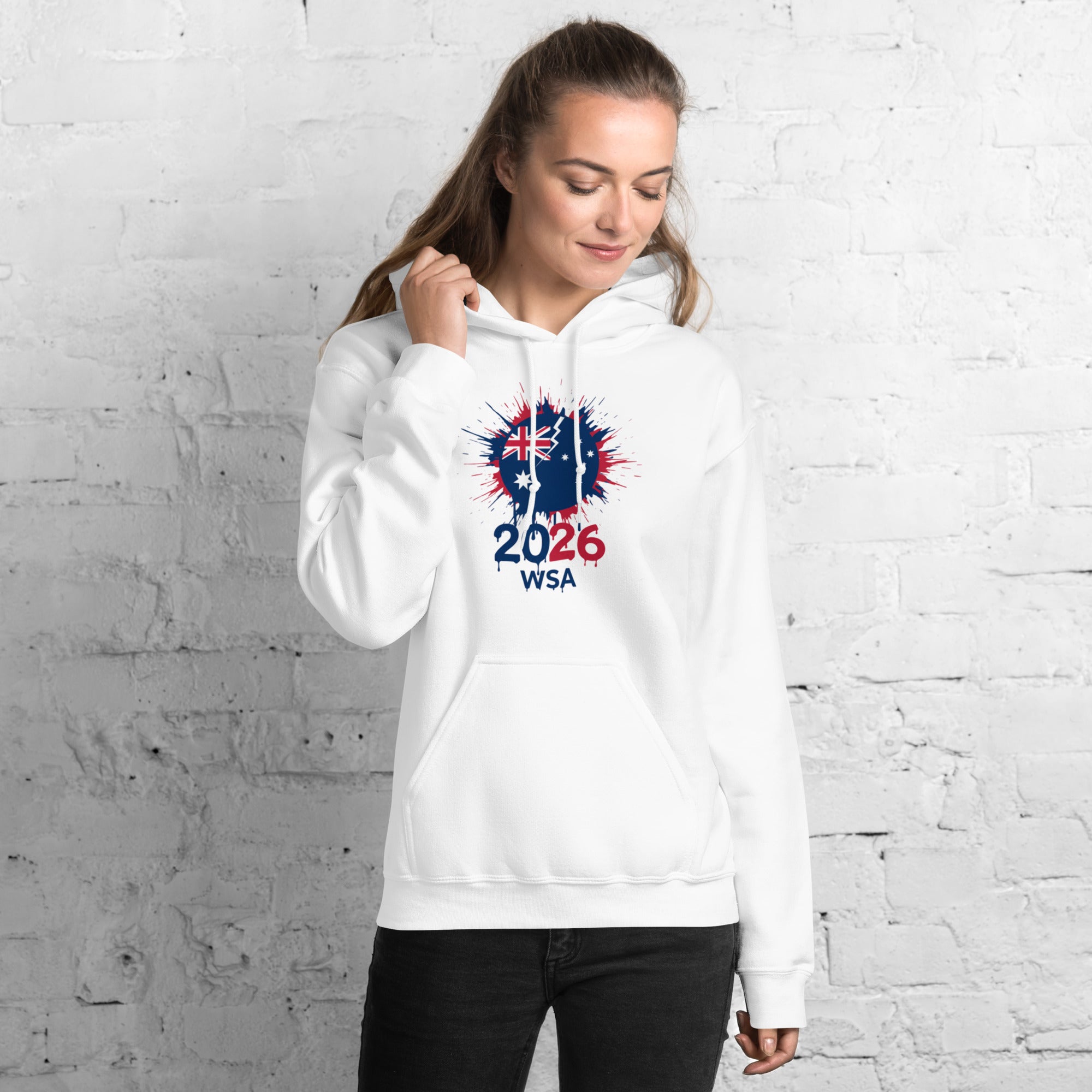 Woman wearing a white hoodie with a design and text against a white brick wall.