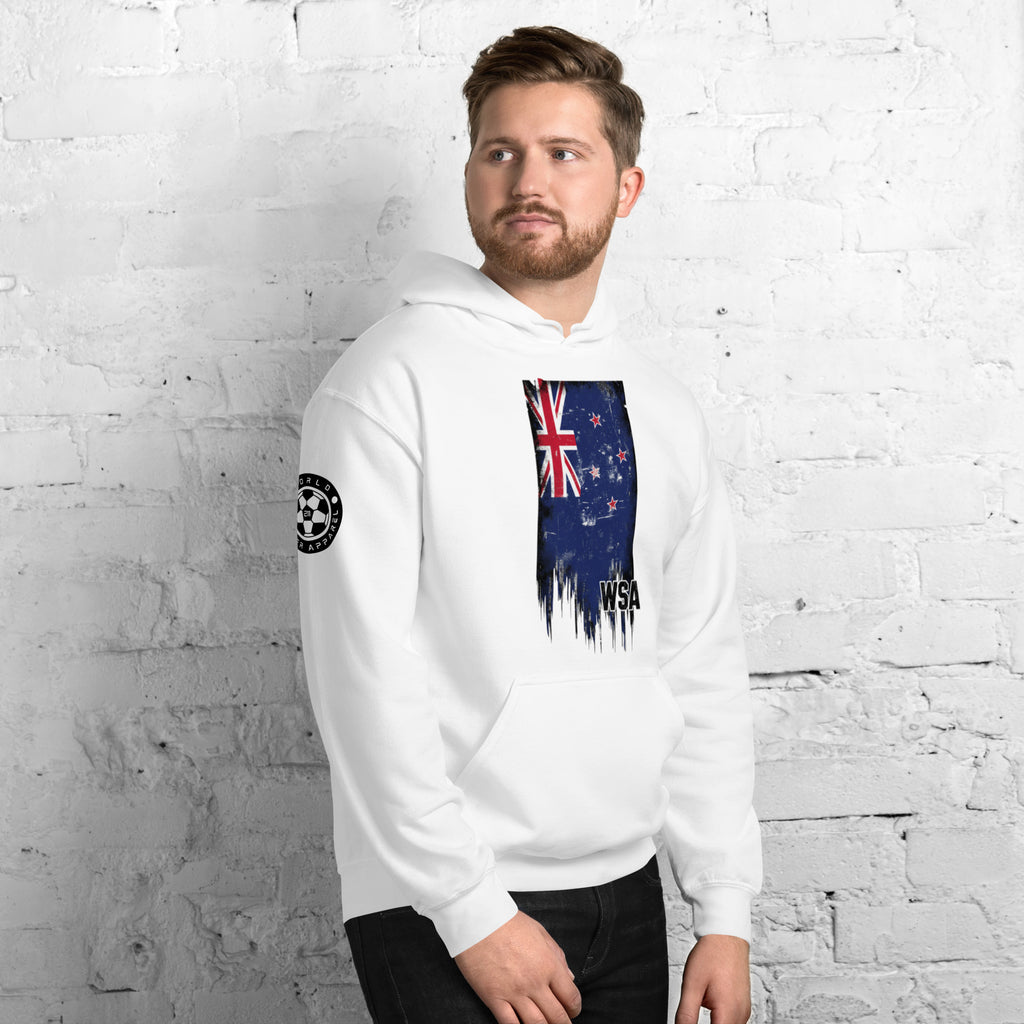 Man wearing a white hoodie with a New Zealand flag design against a white brick wall.