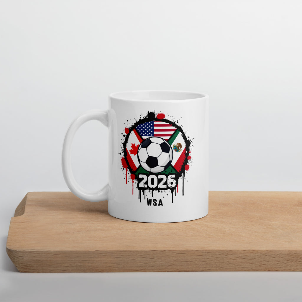 White mug with soccer ball design featuring flags and '2026 WSA' text on a wooden surface.