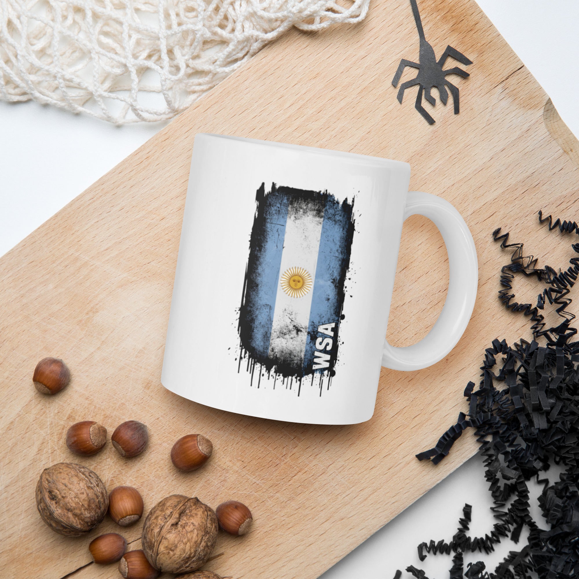 White mug with a flag design on a wooden board with nuts and spider decorations.