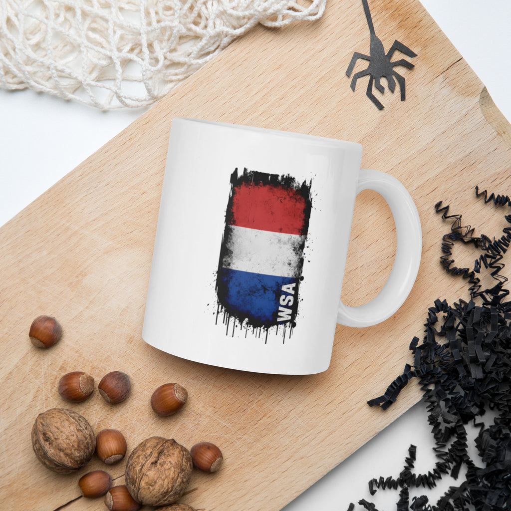 White mug with a flag design on a wooden board with nuts and spider decorations.
