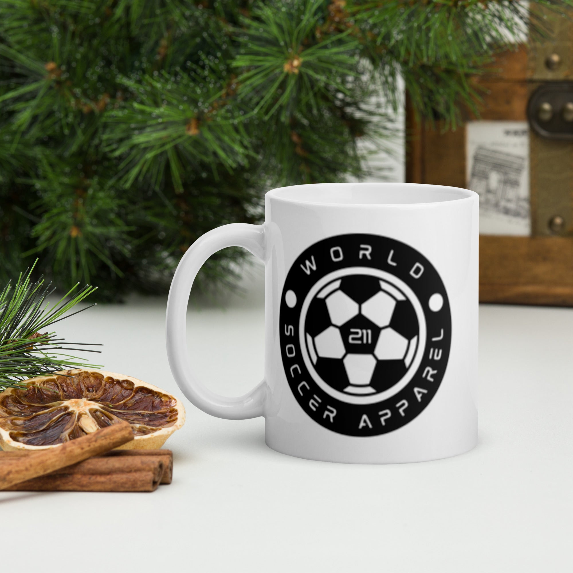 White mug with 'World Soccer Apparel' logo on a table with Christmas decorations.