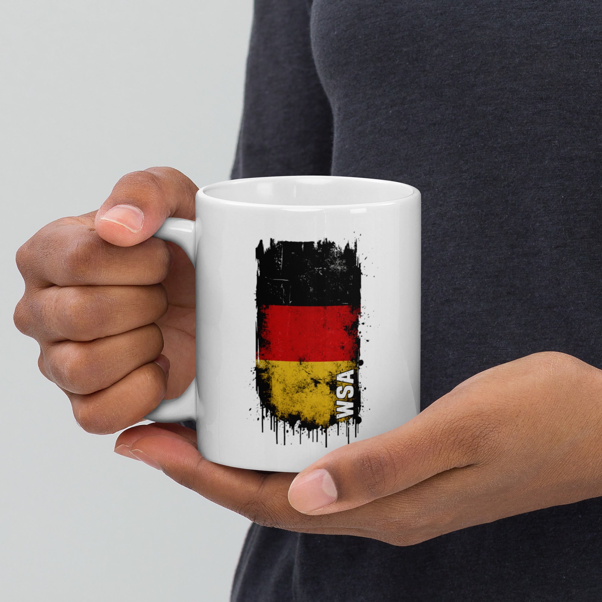Person holding a white mug with a German flag design on a light gray background