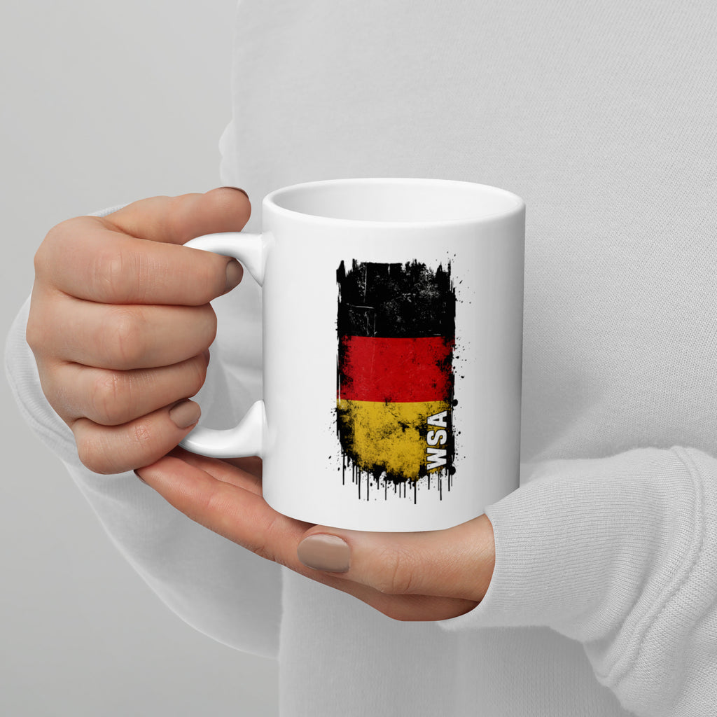 White mug with German flag design held by a person against a gray background