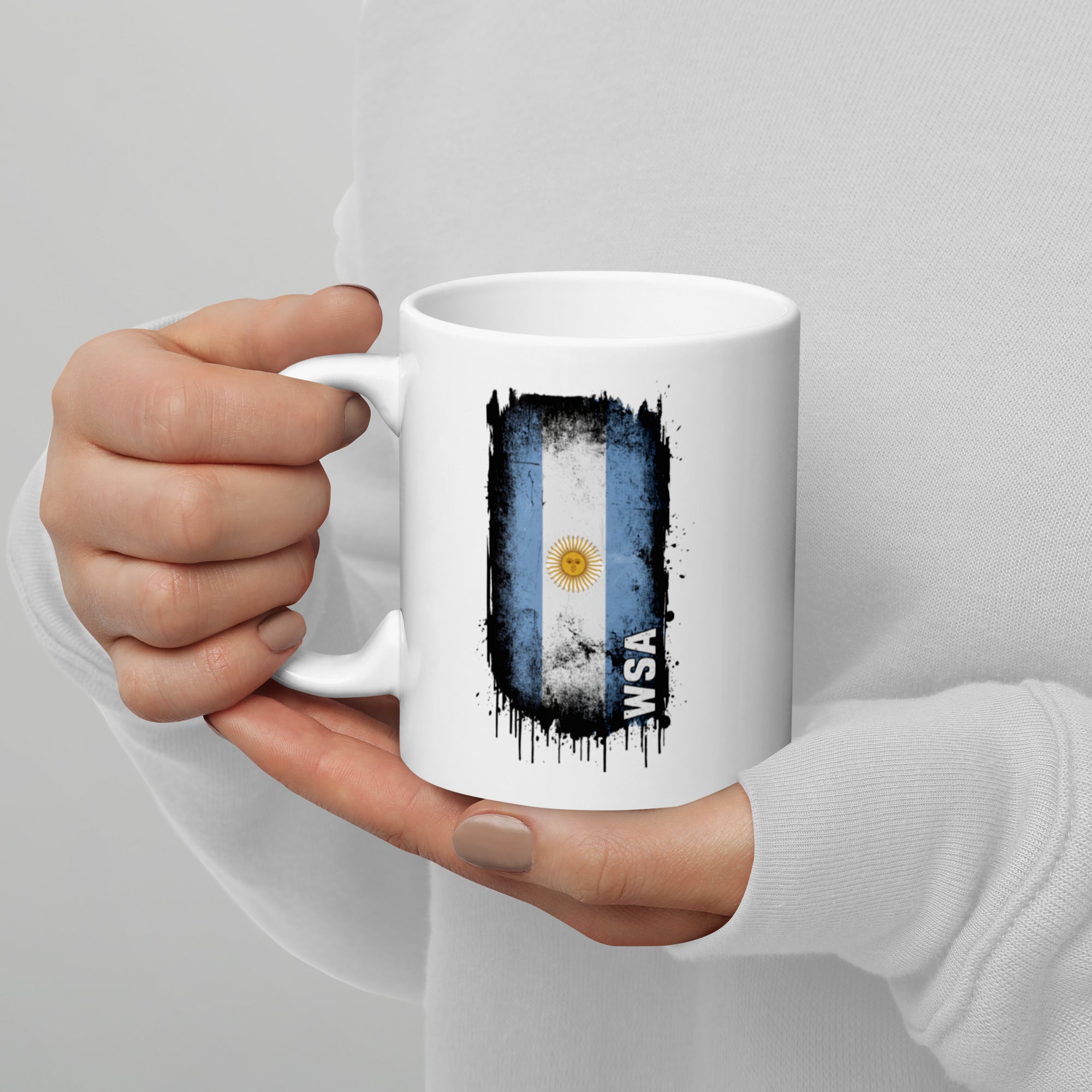 Hand holding a white mug with an Argentina flag design on a gray background