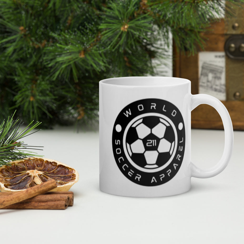 White mug with black logo and text on a white surface with Christmas decorations.