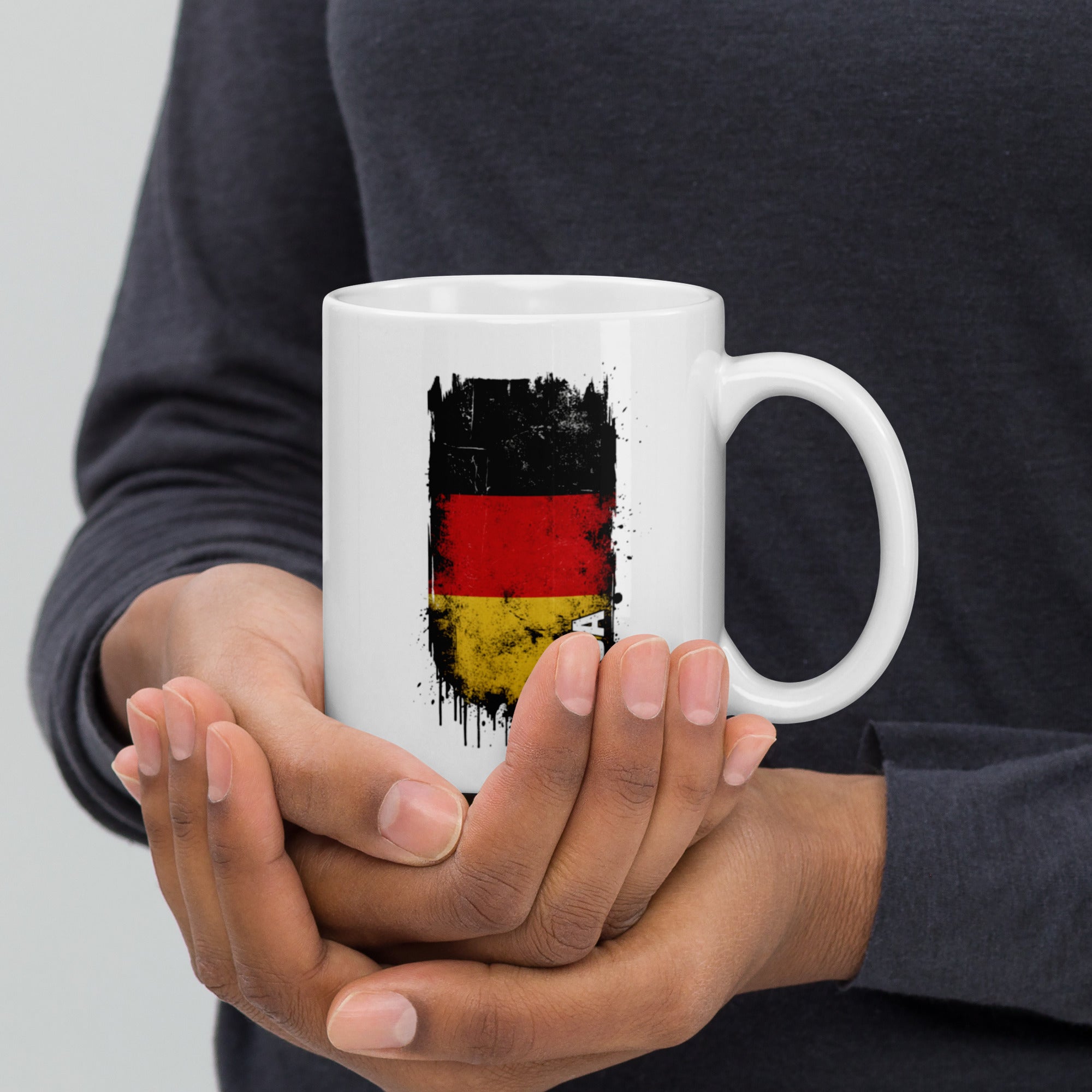 Person holding a white mug with a German flag design.