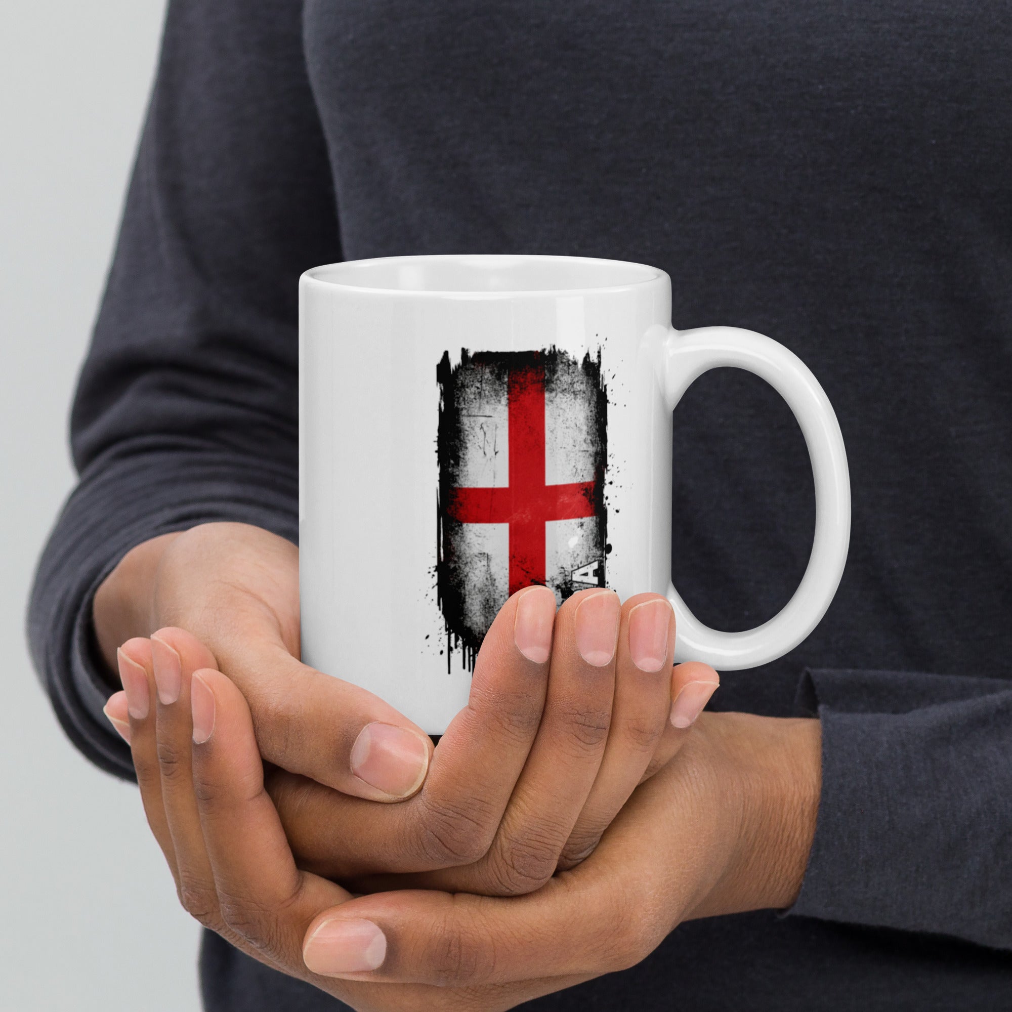Person holding a white mug with a flag design against a gray background