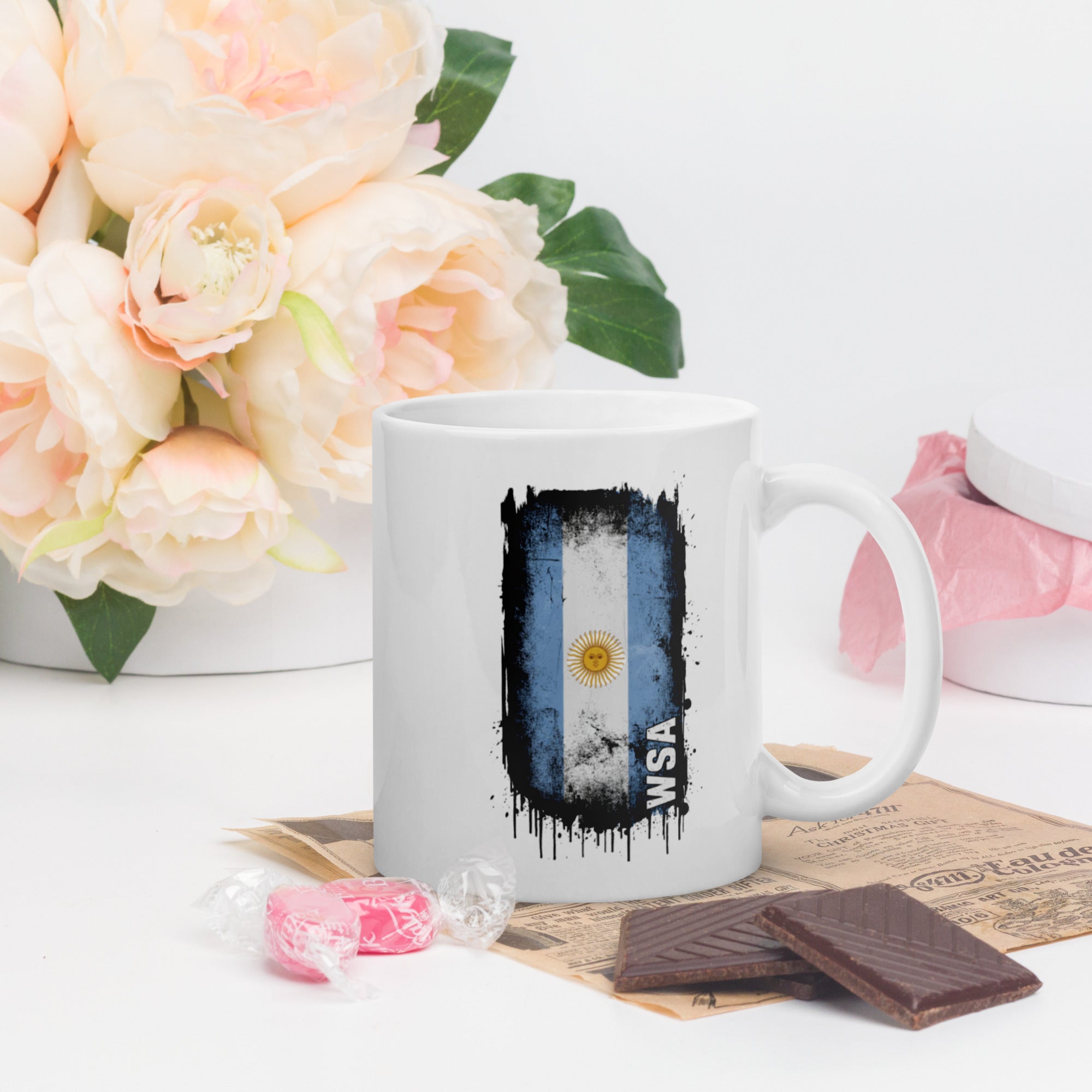 White mug with a flag design on a table with flowers and chocolate