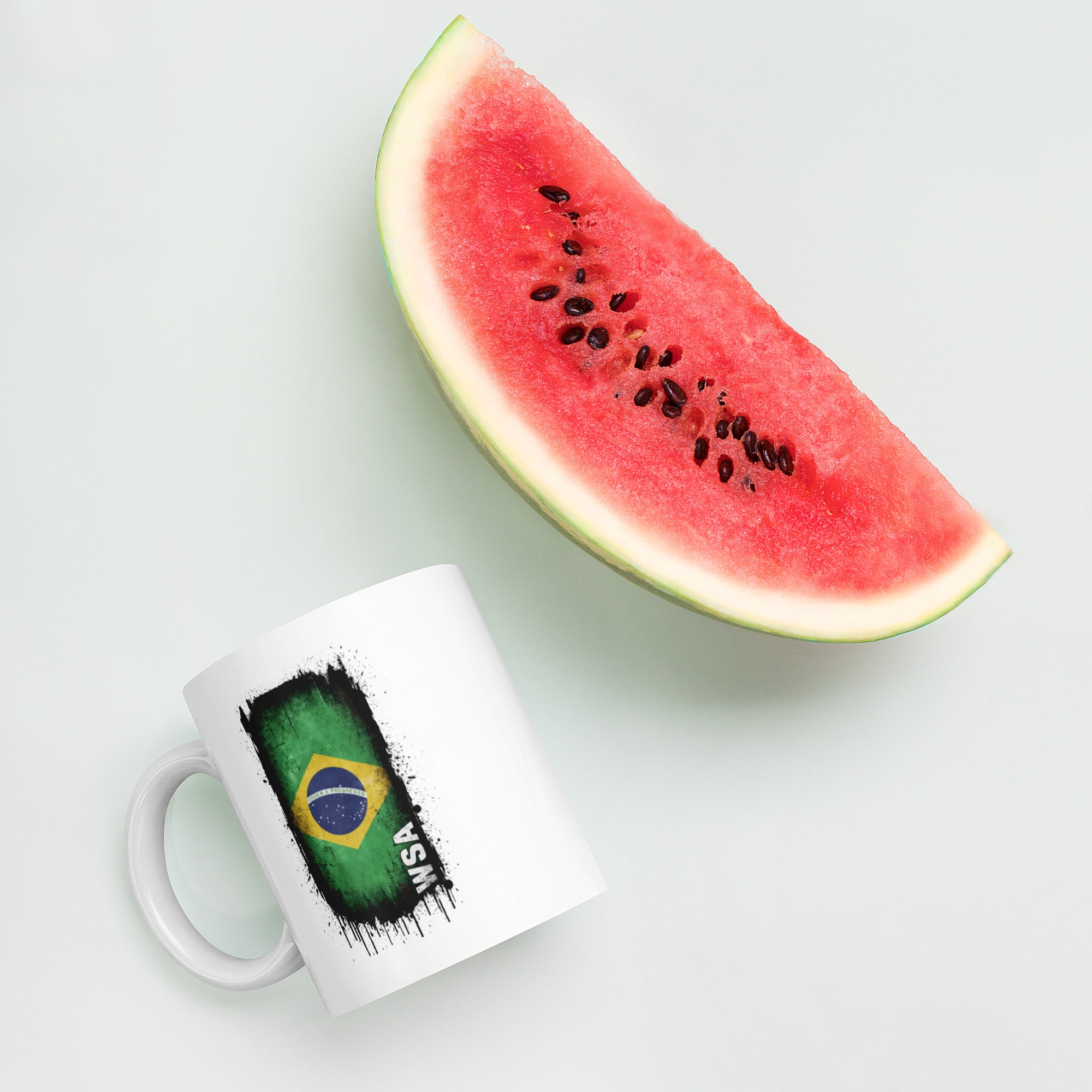 White mug with Brazilian flag design next to a slice of watermelon on a light background