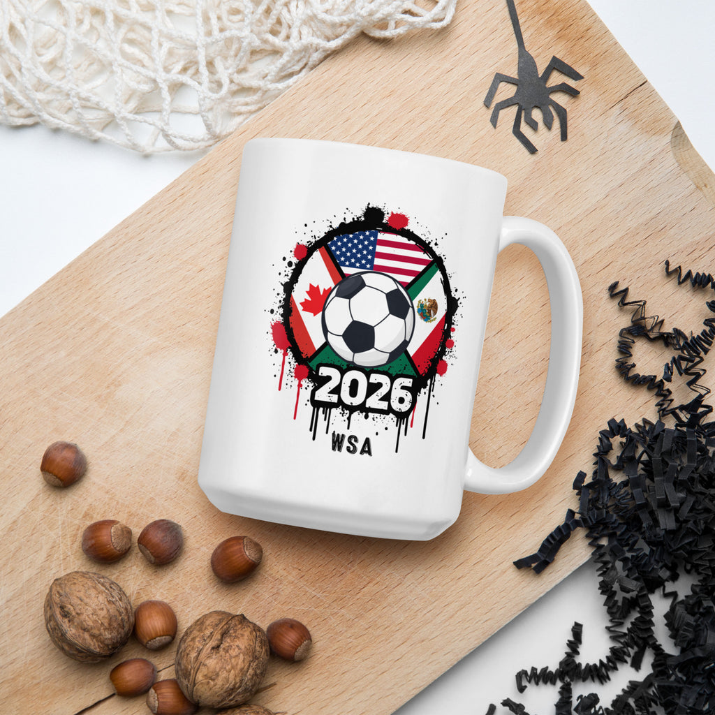 White mug with soccer ball design featuring flags and '2026 WSA' text on a wooden board with nuts and decorative items.