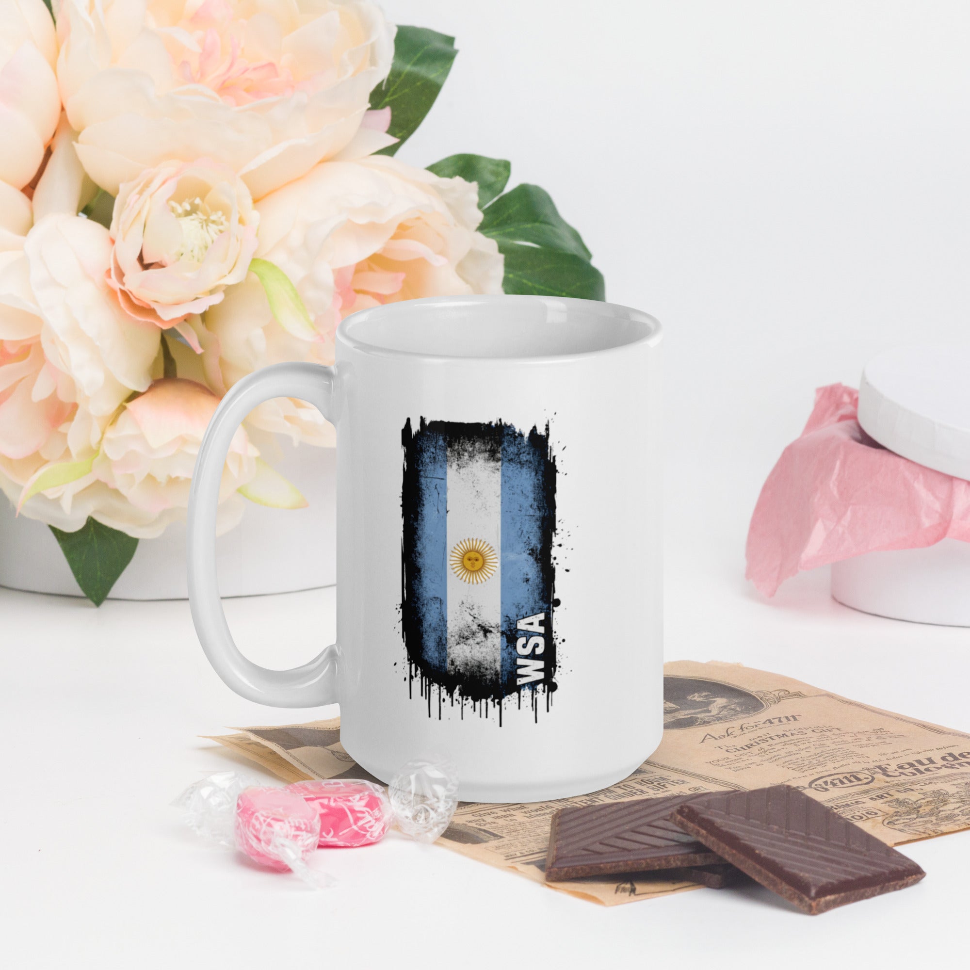 White mug with Argentina flag design on a table with flowers and chocolate