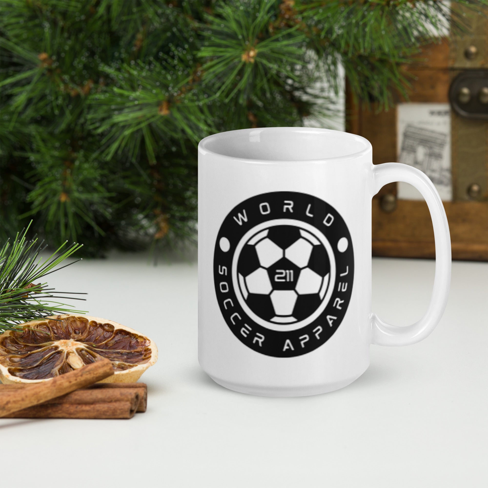 White mug with 'World Soccer Apparel 21' logo on a table with Christmas decorations.