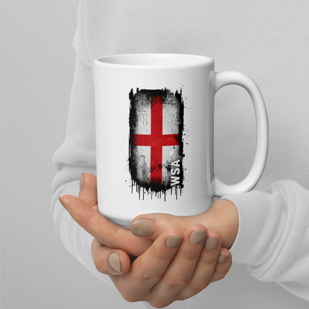White mug with a red and white cross design held by a person against a gray background