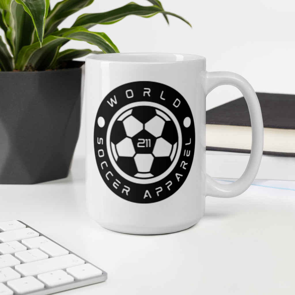 White mug with 'World Soccer Apparel' logo on a desk with a plant and books in the background