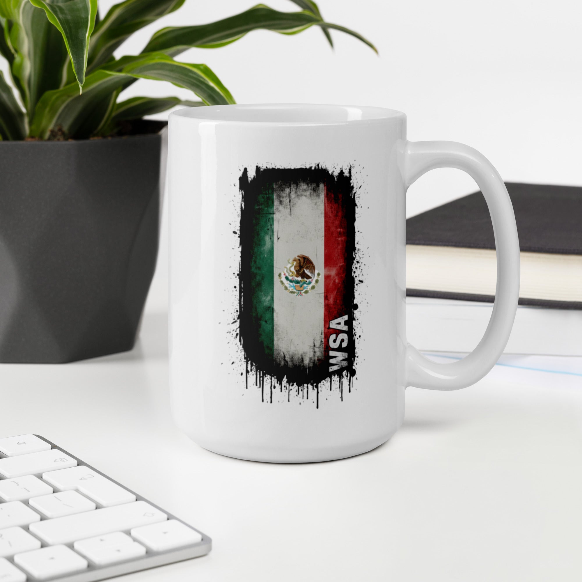 White mug with Mexican flag design on a desk with a keyboard and plant.