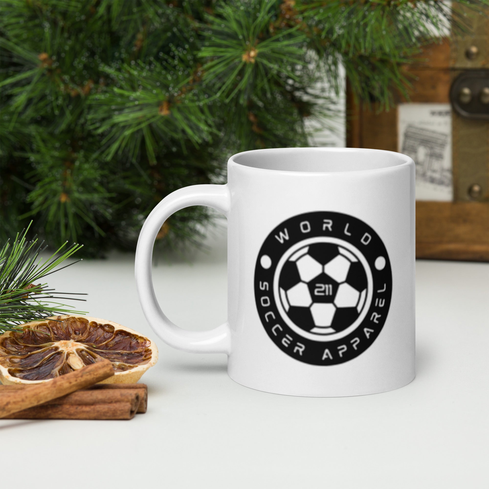 White mug with 'World Soccer Apparel' logo on a surface with Christmas decorations.