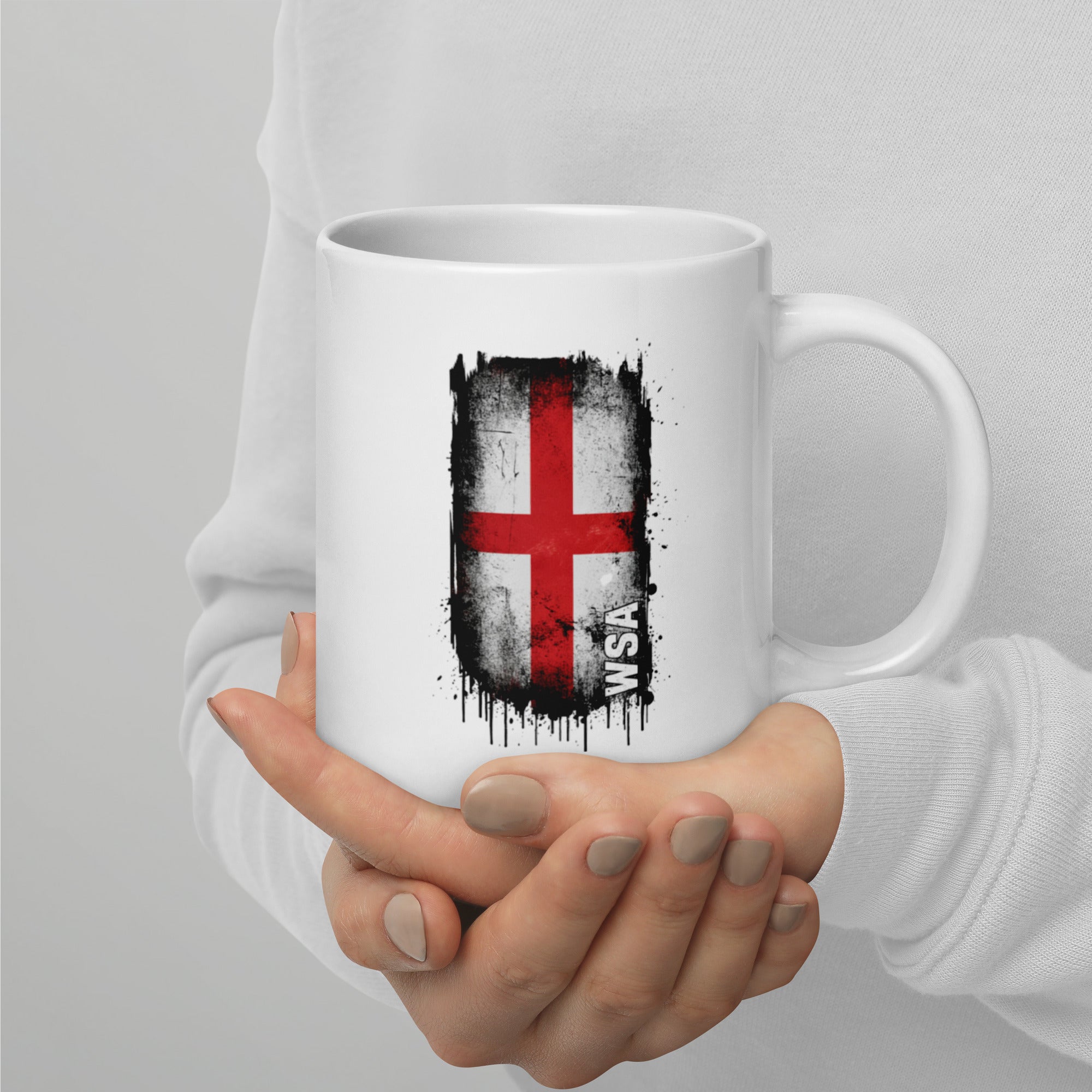 White mug with a red and black design held by a person against a gray background