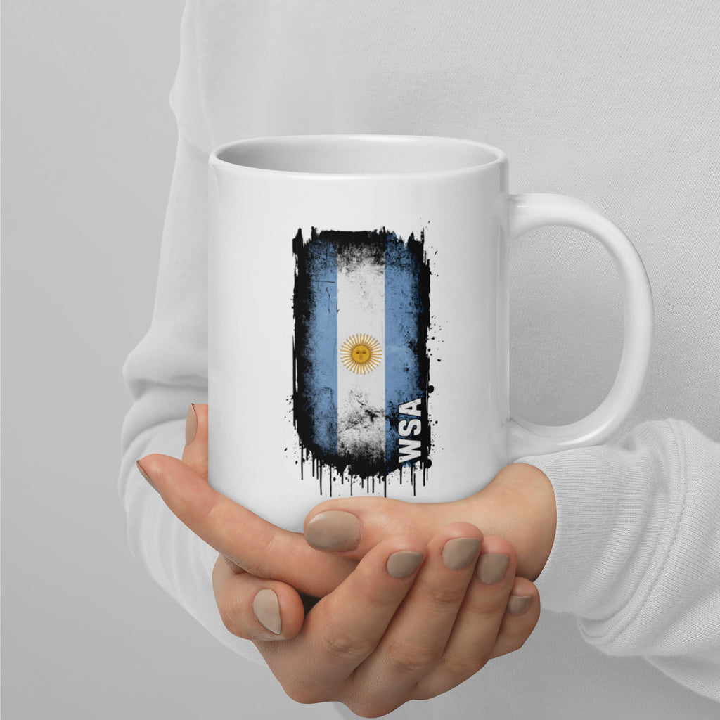 White mug with a flag design held by a person against a gray background