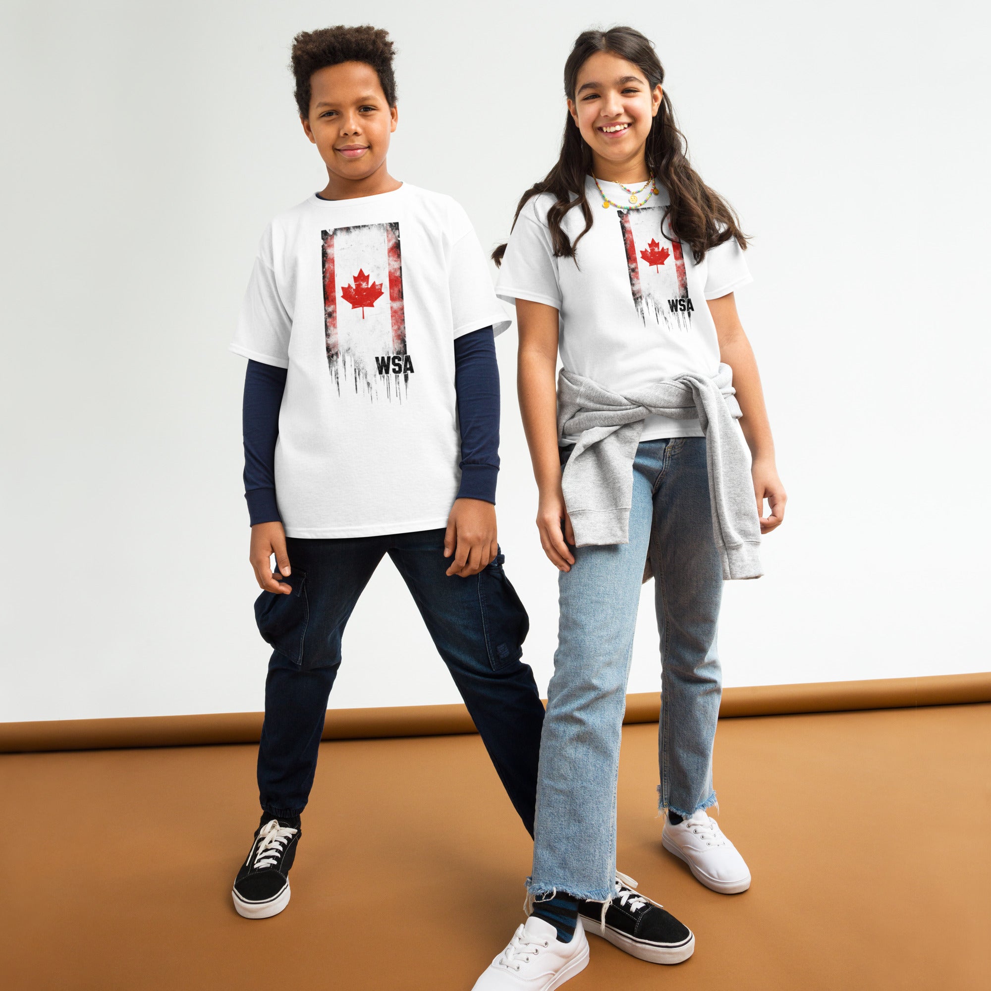 Two children wearing white t-shirts with a red maple leaf design on a plain background