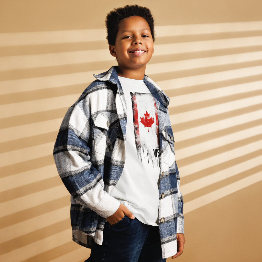 Child wearing a plaid shirt over a graphic t-shirt with a maple leaf design on a striped background